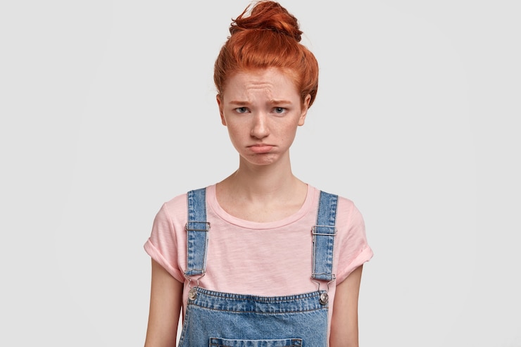 無料Photo 美しい動揺した生姜の若い女性は顔をしかめ、気分を害しているように見える