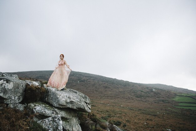 Beautiful vertical picture of a ginger female with a pure white skin in an attractive  pink gown