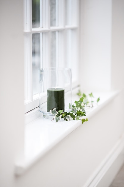 Beautiful vertical shot of a black candle in a glass decorated with leaves on a window shelf