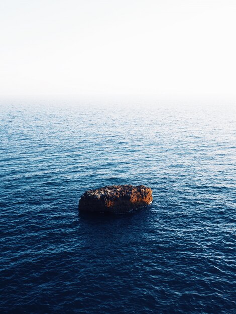 Beautiful vertical shot of a brown rock in the middle of the sea with amazing water textures