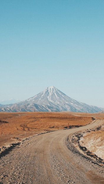 Beautiful vertical shot of a narrow curvy and muddy road with a high mountain