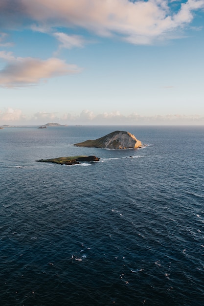 Beautiful vertical shot of small hills in the sea under the cloudy sky during daytime