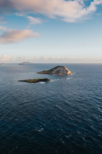 Beautiful vertical shot of small hills in the sea under the cloudy sky during daytime