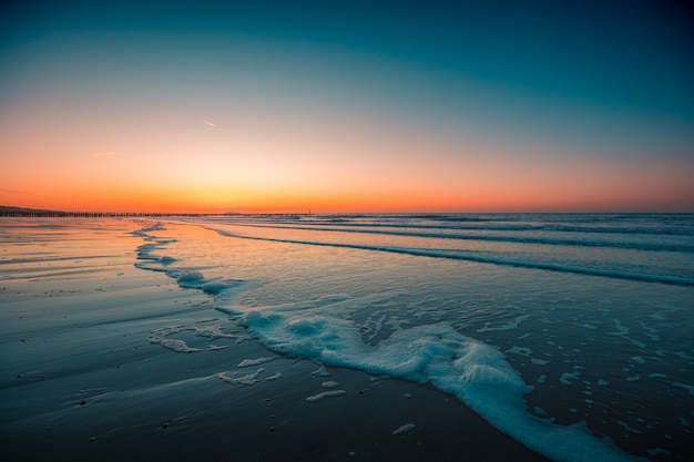 Domburg, 네덜란드에서 캡처 한 석양 아래 해변에서 거품 파도의 아름 다운보기