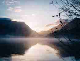 Free photo beautiful view of a lake surrounded by mountains with a glowing sun in the background