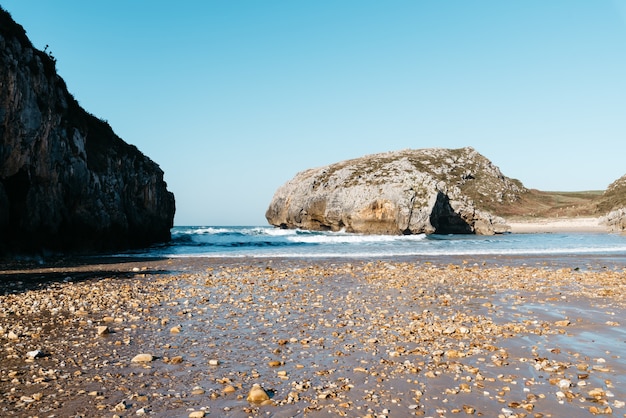 Free photo beautiful view of the ocean waves crashing on the rocks near the beach under a blue sky