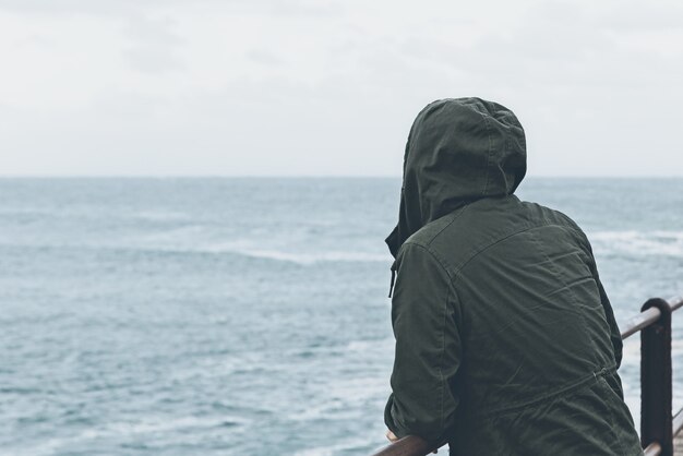 Прекрасный вид человека, стоящего на причале и смотрящего на океан в пасмурную погоду