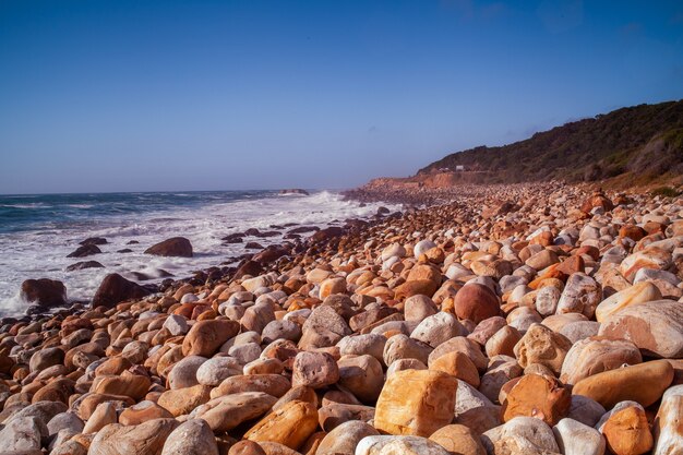 Beautiful view of the rocks on the beach by the sea under the clear blue sky