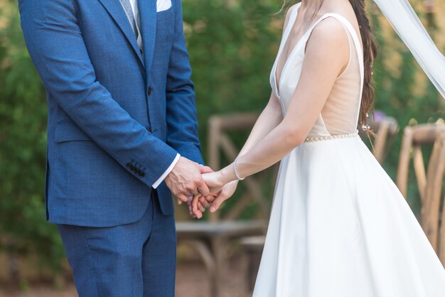 Красивый вид на романтическую невесту и жениха, держась за руки на своей свадьбе