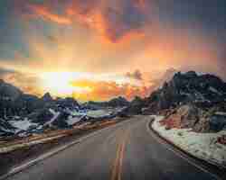 Free photo beautiful vista of a narrow countryside road with rocky mountains covered in snow in the distance