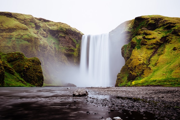 Красивый водопад между зелеными холмами в Skogafoss, Исландия