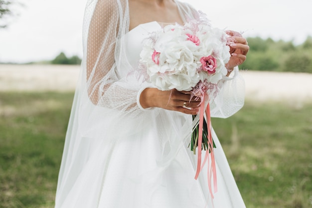 Красивый свадебный букет из белых нарциссов с розовыми серединками в руках невесты на природе