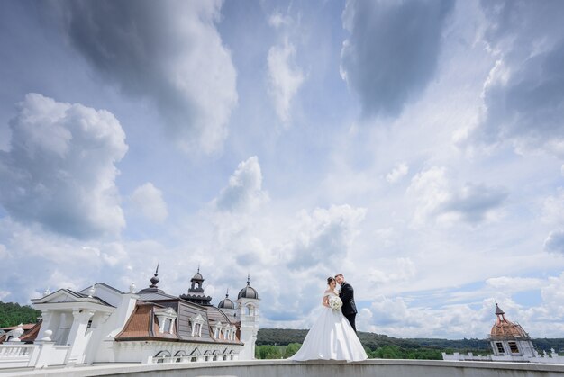 Beautiful wedding couple is standing near the church with beautiful cloudy sky