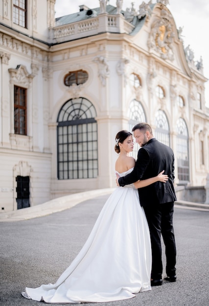 Beautiful wedding couple in love is standing together in front of historical architectural building