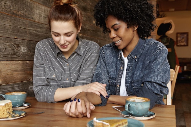 Beautiful white lesbian with hair bun talking to her fashionable black girlfriend in trendy denim jacket