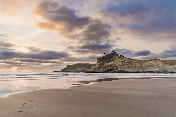 Free Photo beautiful wide shot of a cliff by the sea with a sandy shore under a sky with clouds