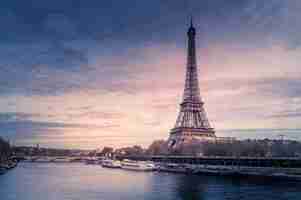 Free photo beautiful wide shot of eiffel tower in paris surrounded by water with ships under the colorful sky