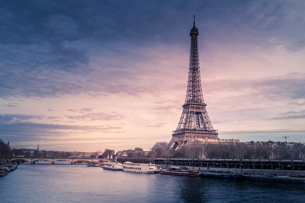 Beautiful wide shot of Eiffel Tower in Paris surrounded by water with ships under the colorful sky