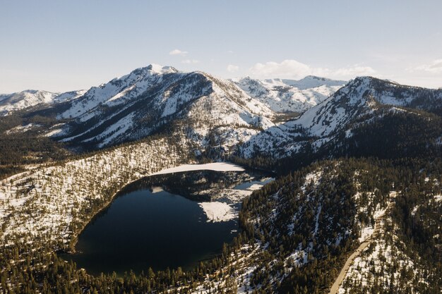 Beautiful wide shot of mountains covered with snow surrounded by trees and a lake