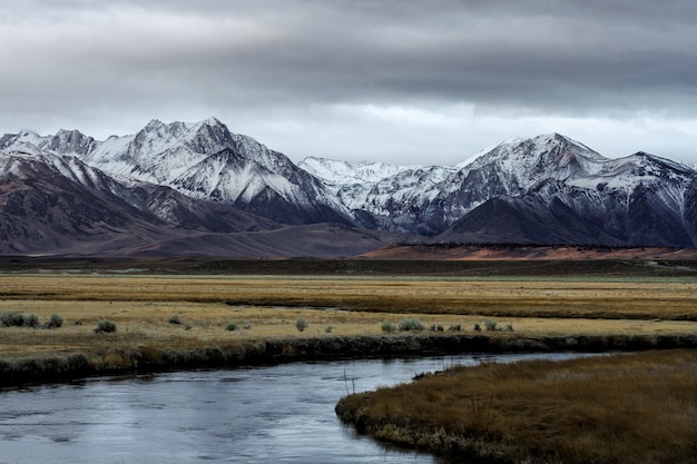 Beautiful wide shot of mountains surrounded by a river and flat grass fields