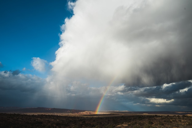 Beautiful wide shot of a rainbow among white clouds in a clear blue sky