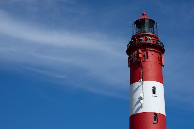 Beautiful wide shot of the top of a red and white lighthouse tower on a sunny day at the beach