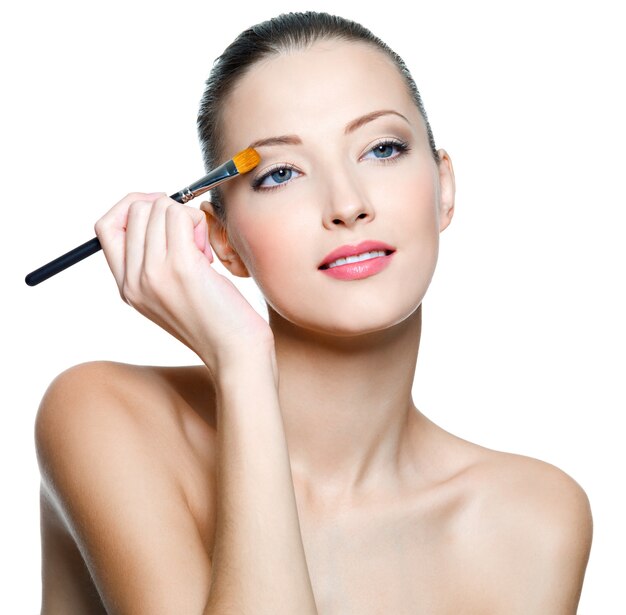Beautiful woman applying eyeshadow with brush isolated on white