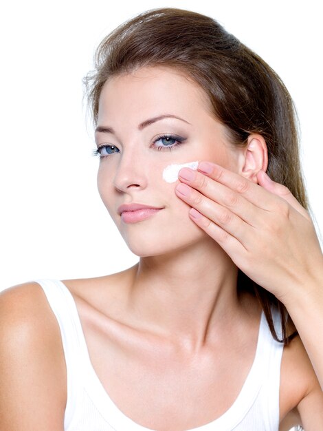 Beautiful woman applying moisturizer cosmetic cream on face isolated on white