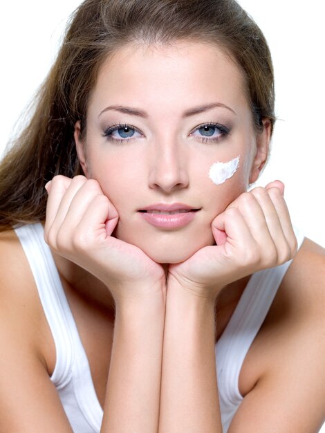 Beautiful woman applying moisturizer cream on face - on a white