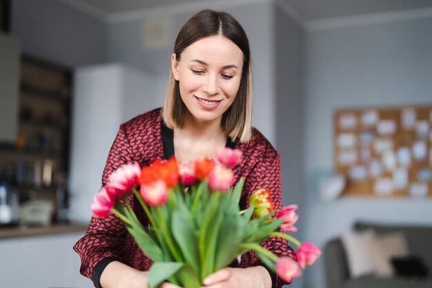 Beautiful woman arranging flowers presented by her husbant at home happy and joyful