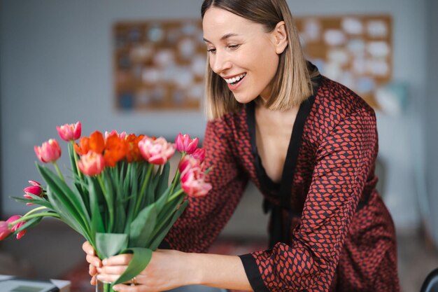 Красивая женщина расставляет цветы, подаренные мужем дома, счастливая и радостная