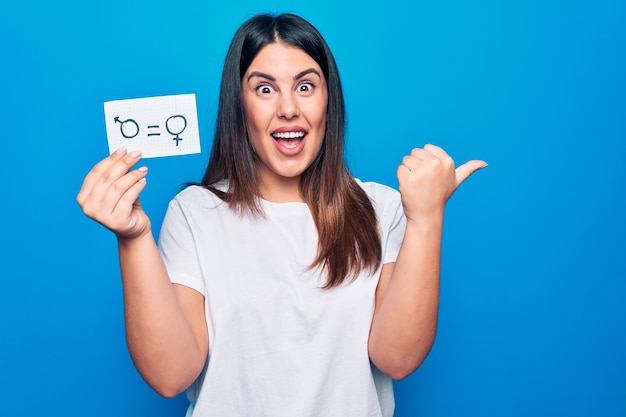 Free photo beautiful woman asking for sex discrimination holding paper with gender equality concept pointing thumb up to the side smiling happy with open mouth