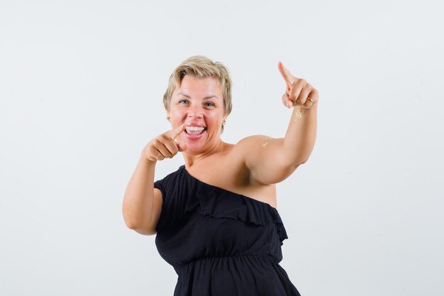 Free photo beautiful woman in black blouse pointing at front and looking amused