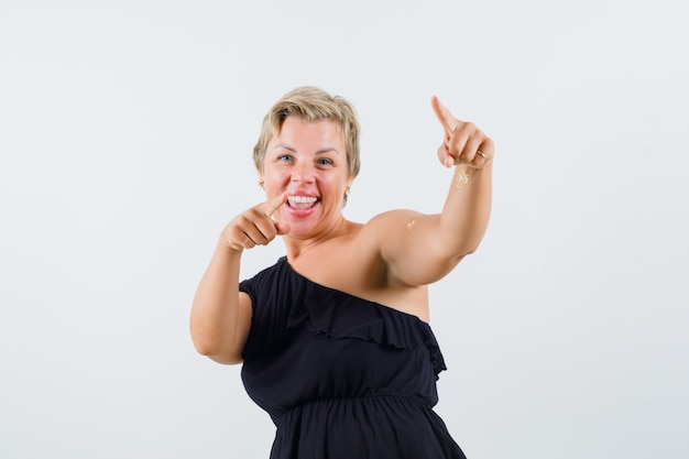 Beautiful woman in black blouse pointing at front and looking amused