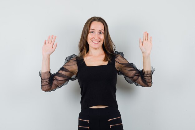Beautiful woman in black blouse raising hands up and looking merry 
