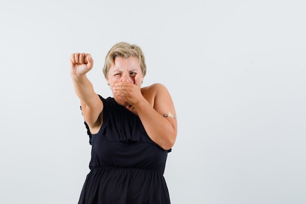 Beautiful woman in black blouse showing her power with raised arm while holding hand on mouth and looking angry