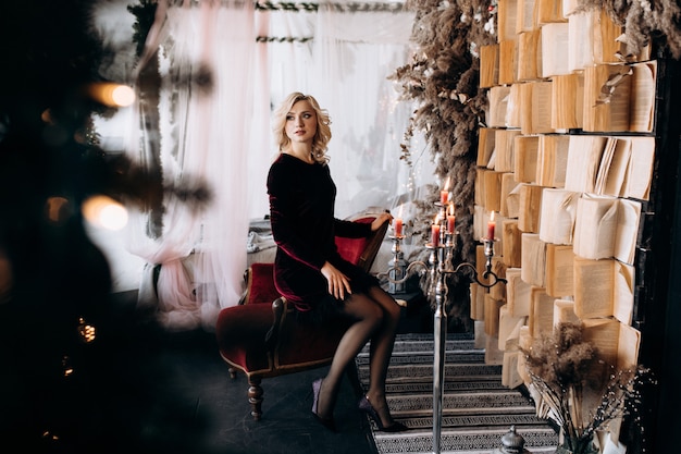 Beautiful woman in black dress sits before a wall of books and Christmas decor