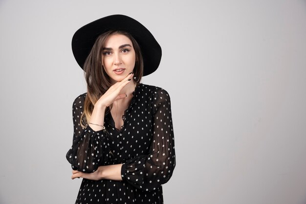 Beautiful woman in black hat holding her chin.