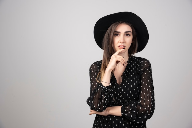 Beautiful woman in black hat standing on gray.