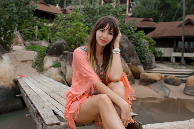 Красивая женщина в платье Бохо позирует возле роскошного курорта. Наслаждаемся отдыхом на тропическом острове.