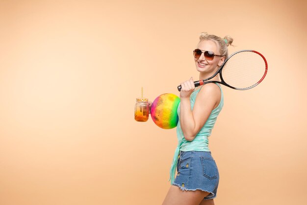 A beautiful woman in a bright outfit denim shorts with a racket in her hands in the studio Summer