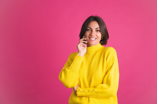 밝은 노란색 스웨터에 아름 다운 여자는 자신감이 미소로 앞으로 분홍색 모습에 고립
