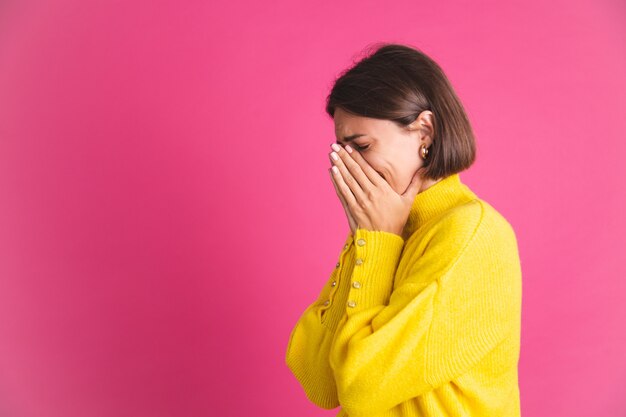 ピンクのストレスの多い泣いているうつ病に分離された明るい黄色のセーターを着た美しい女性