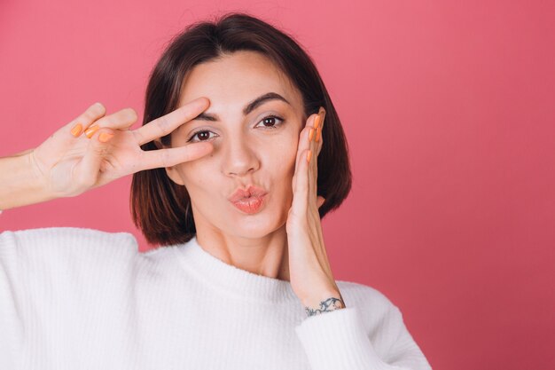 Beautiful woman in casual white sweater, does victory gesture send air kiss 