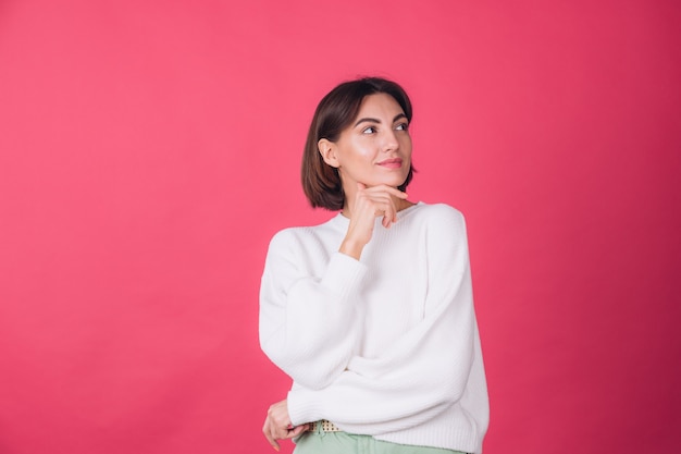 Beautiful woman in casual white sweater on red wall