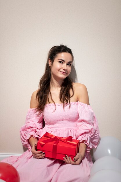 Beautiful woman celebrating valentines day in a pink dress with balloons and present