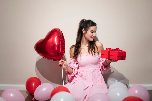 風船とプレゼントのピンクのドレスでバレンタインデーを祝う美しい女性