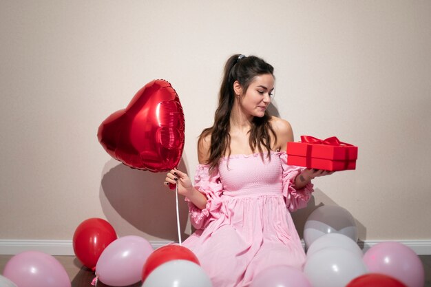 Beautiful woman celebrating valentines day in a pink dress with balloons and present