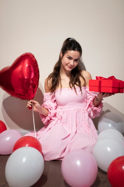 Beautiful woman celebrating valentines day in a pink dress with balloons and present