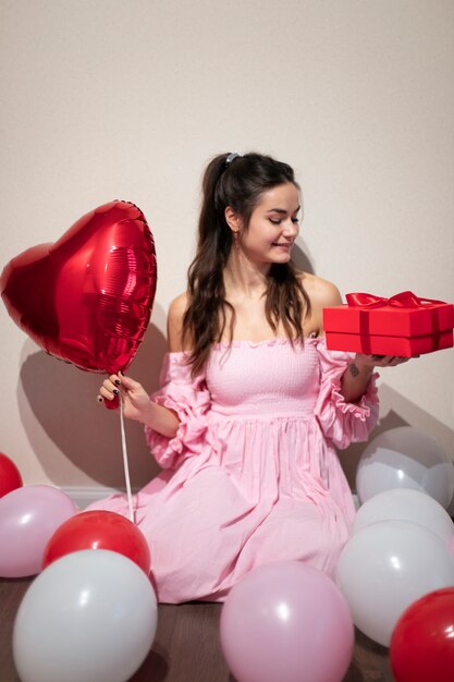 Beautiful woman celebrating valentines day in a pink dress with balloons and present